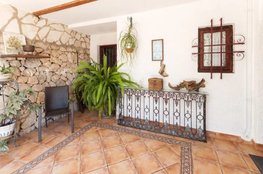 A tiled indoor sitting area features a stone wall, potted plants, and decorative metal railing.