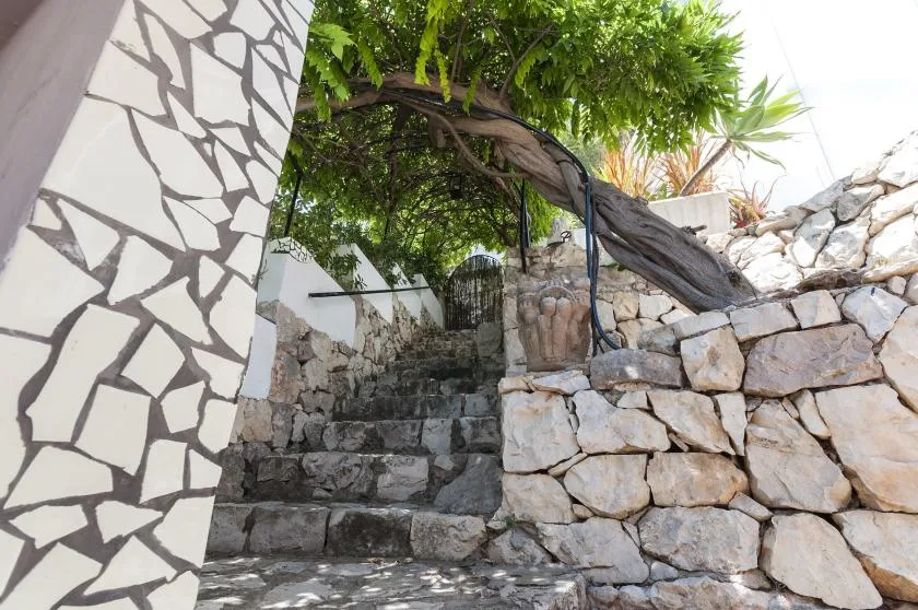 A stone stairway rises between stone walls beneath leafy trees.