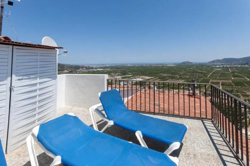 A rooftop terrace with blue sun loungers overlooks fields and distant hills.