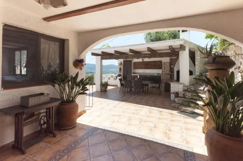 A covered patio opens onto an outdoor dining area, with potted plants nearby.