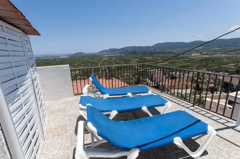 A rooftop terrace with blue lounge chairs overlooking a valley and hills.