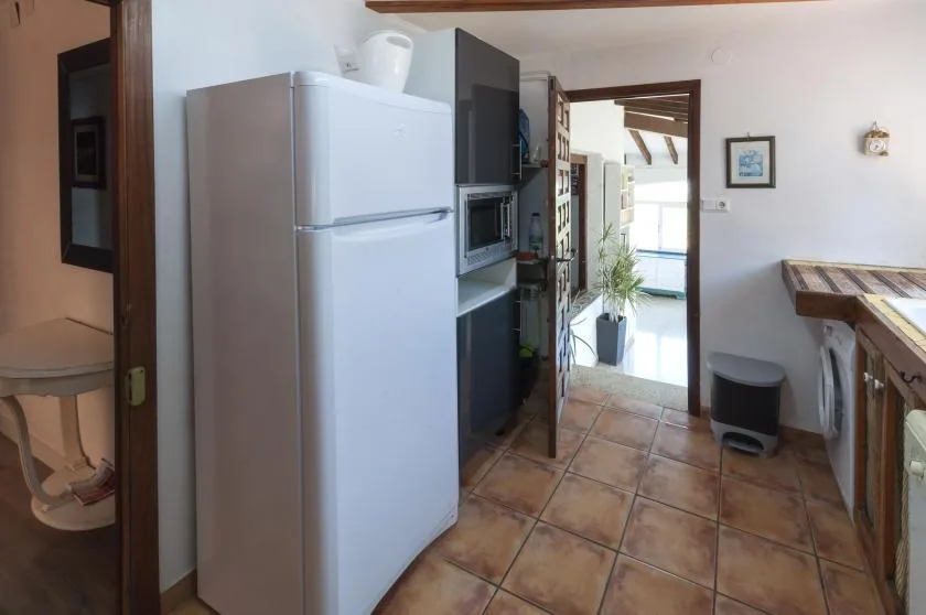 A kitchen with a refrigerator and counter opens onto a bright adjoining room.