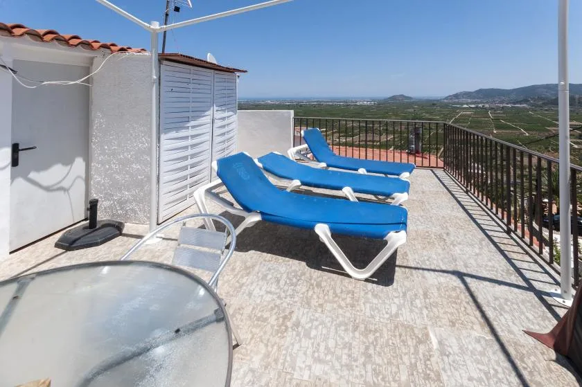 A sunny terrace with blue loungers and a view across the surrounding landscape.