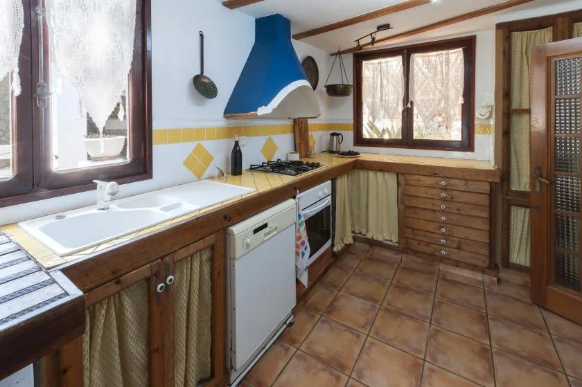 A kitchen with a sink, stove, and wooden cabinets beneath a window.