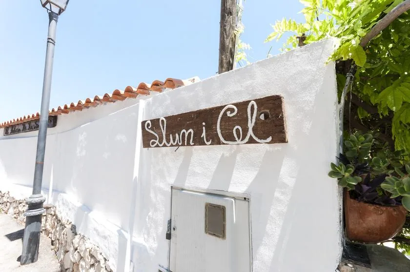 A white exterior wall has a small door beneath a wooden sign.