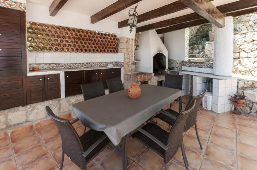 A tiled outdoor dining area with a long table and built-in barbecue.