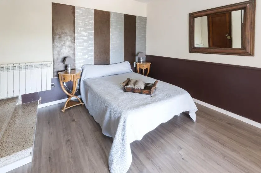 A bedroom with a neatly made bed and a framed mirror on the wall.