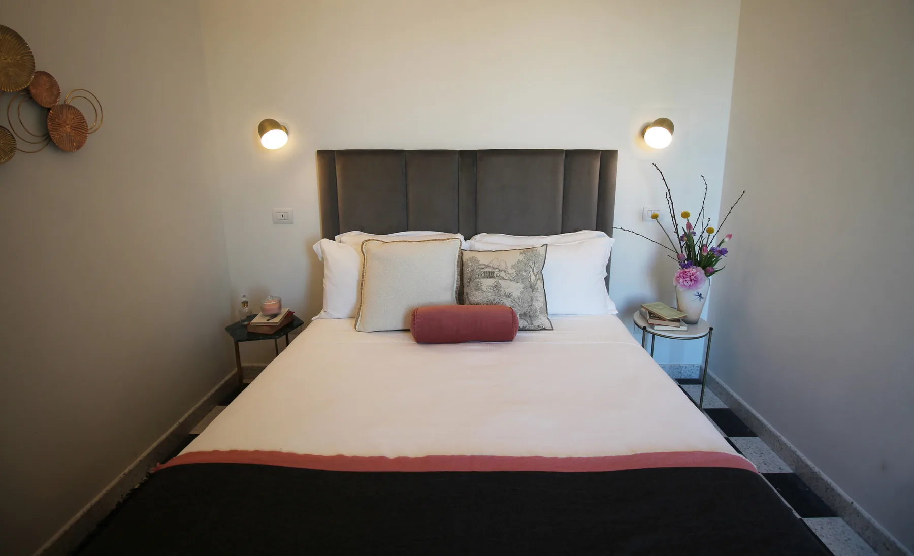 Un dormitorio con una cama bien tendida y luces de pared a ambos lados.