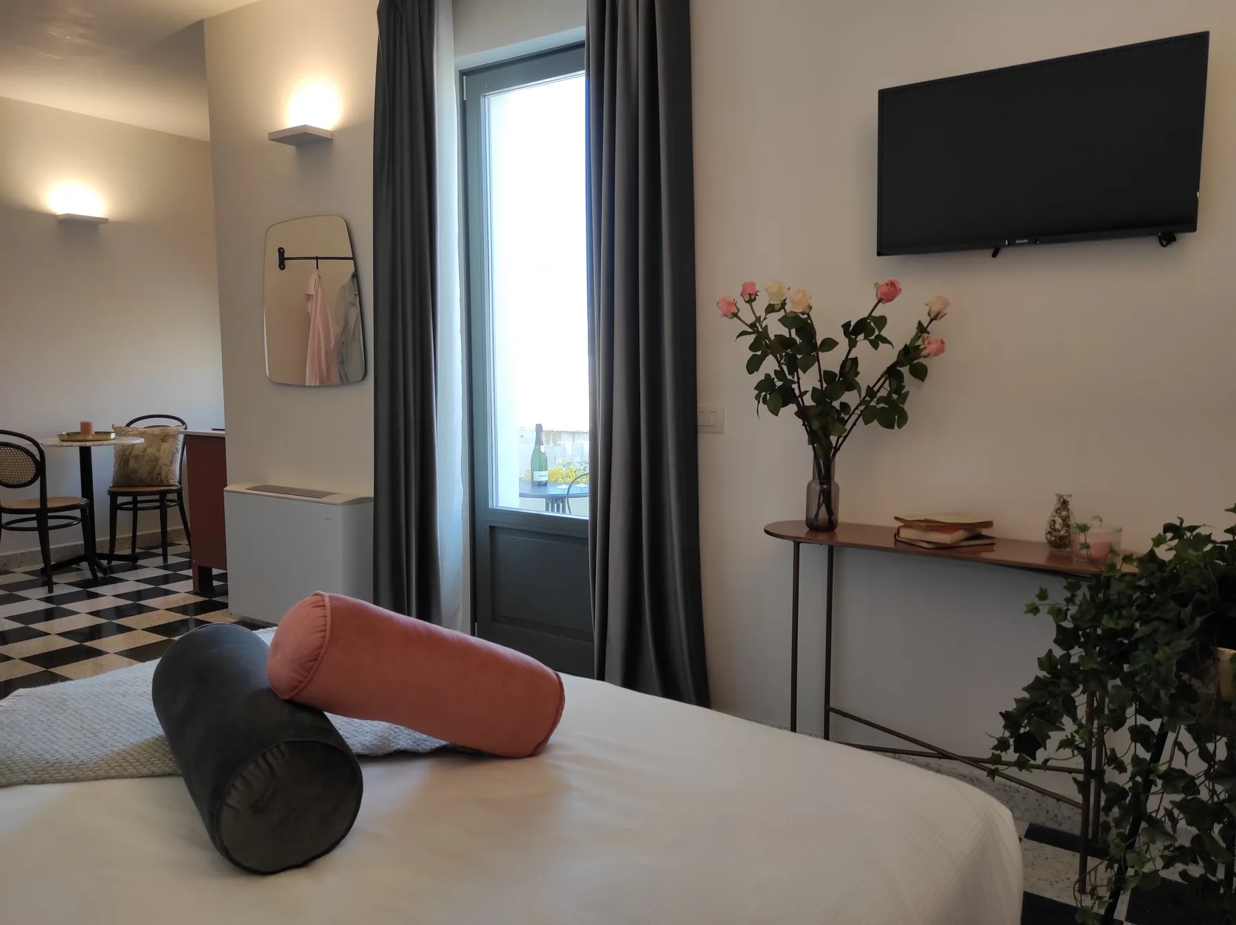 Un dormitorio con una cama, cortinas oscuras y un televisor en la pared.
