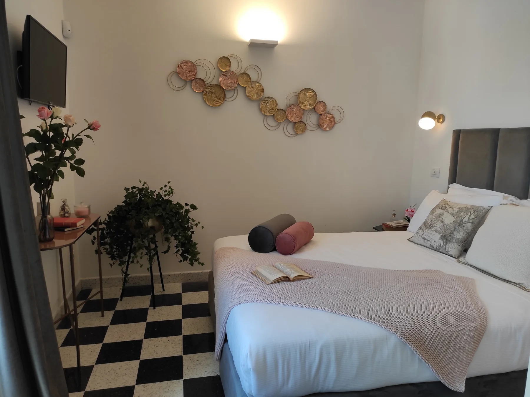 Un dormitorio con una cama bien hecha, arte decorativo en la pared y un suelo a cuadros.