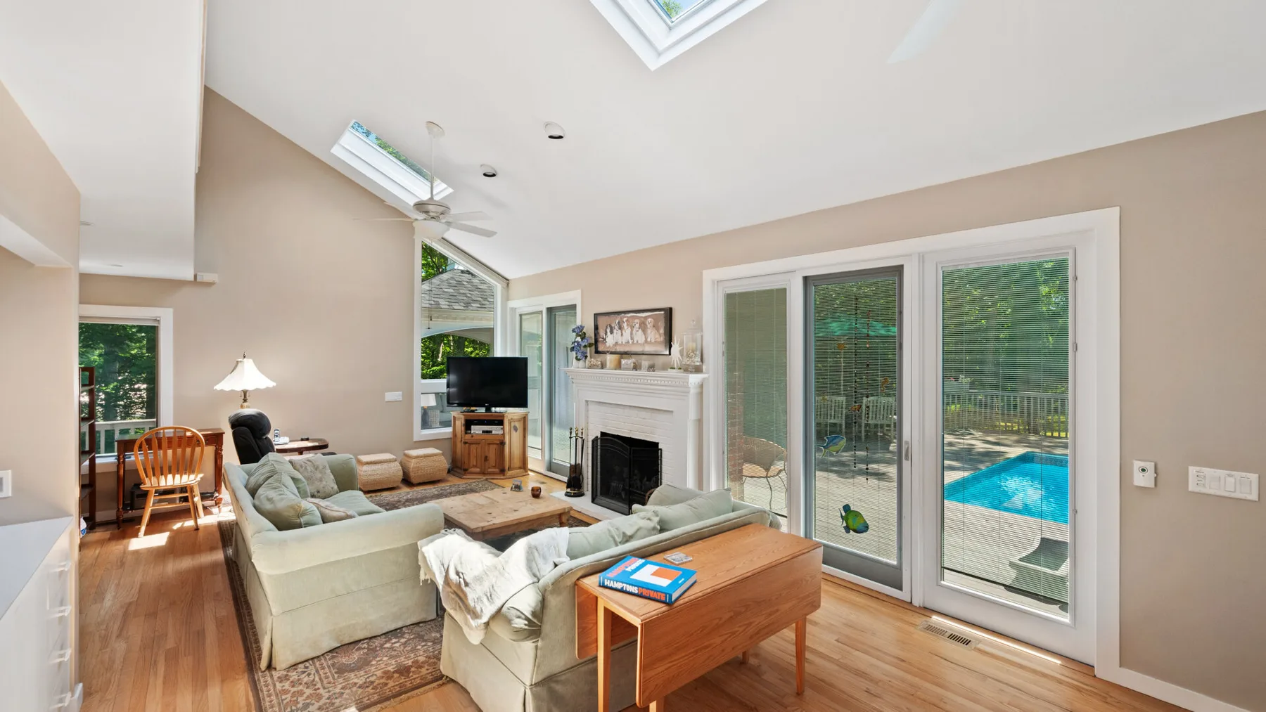 A bright living room with seating, large windows, and a view of a pool.