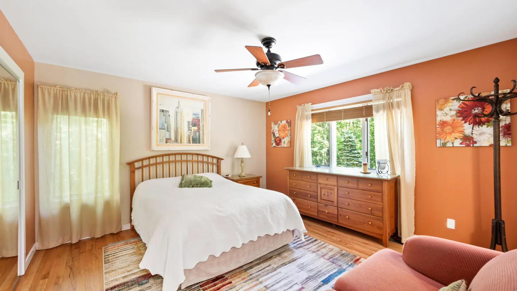 A bedroom with a bed, wooden dresser, and windows with sheer curtains.