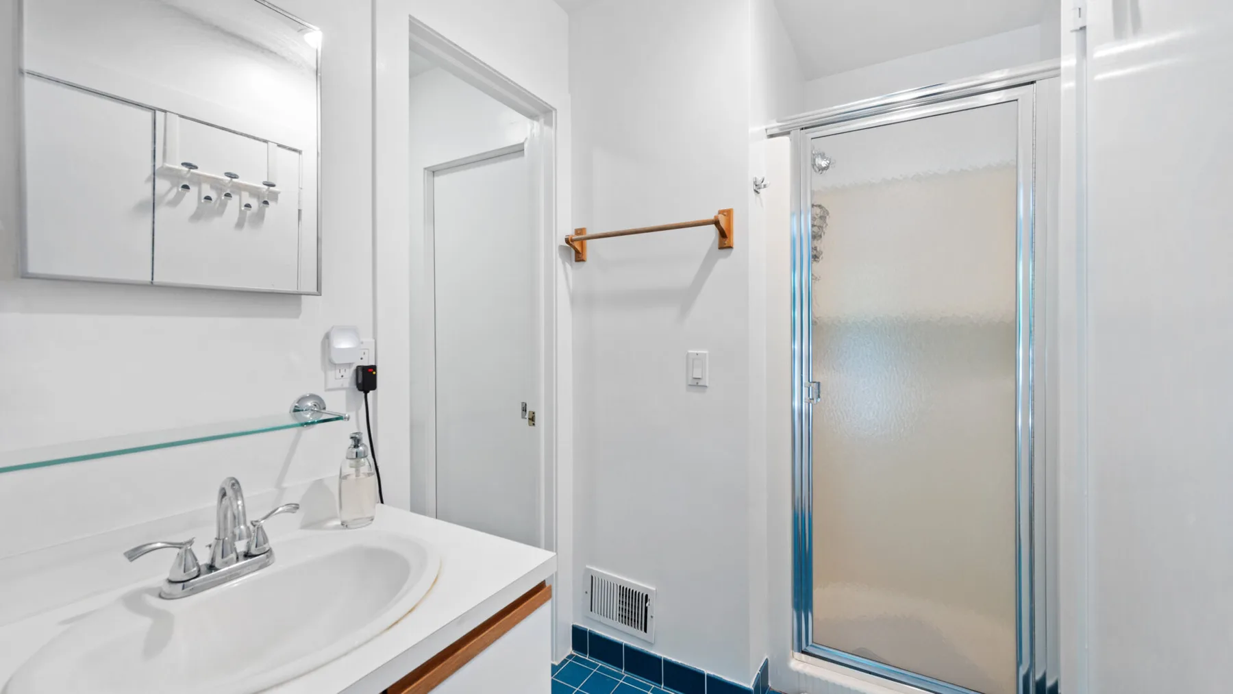 A bright bathroom with a sink, wall mirror, and glass shower.