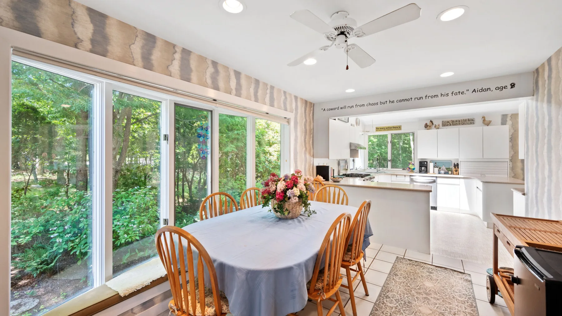A dining area with a table beside large windows, opening onto a kitchen.