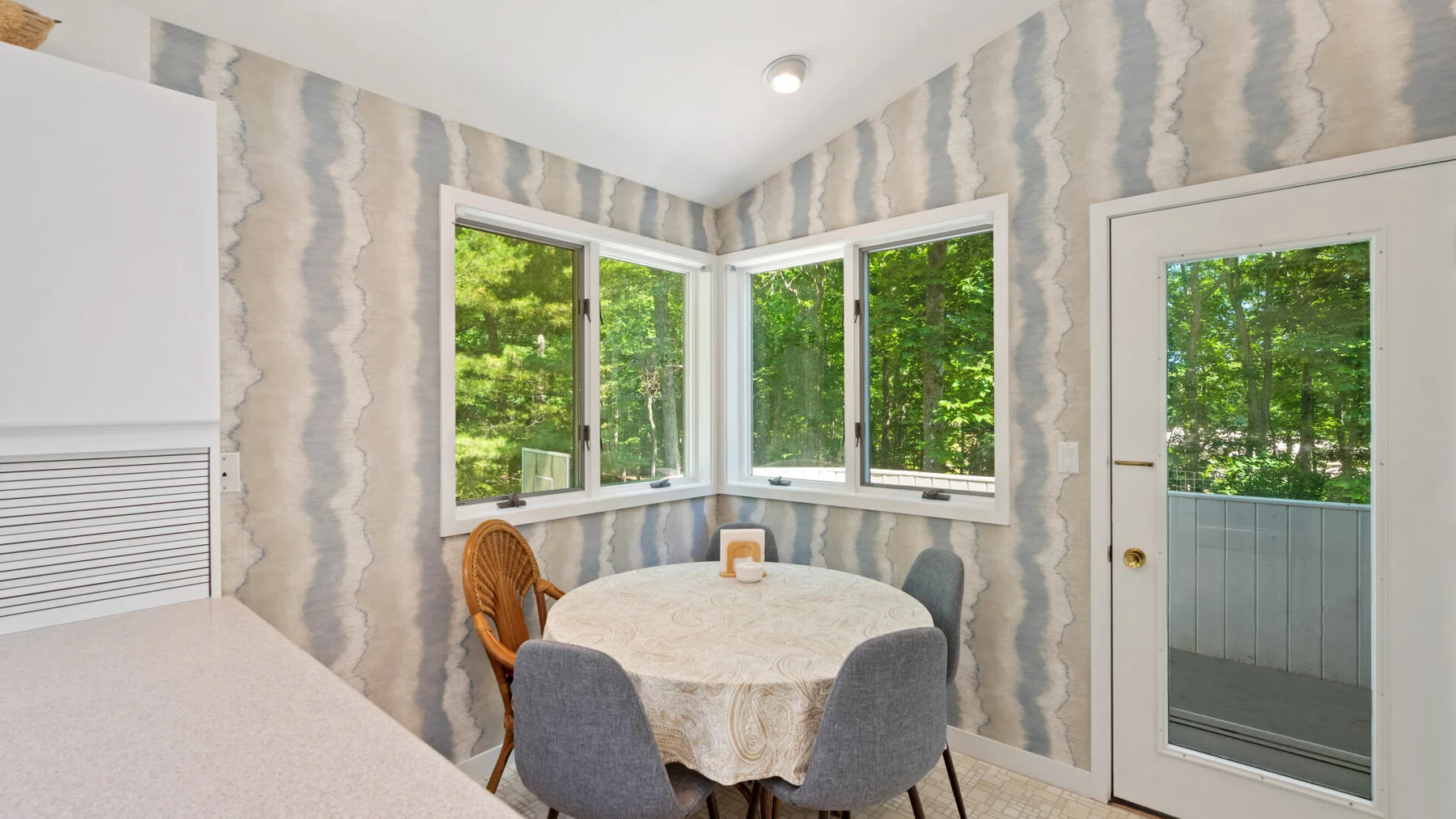 A small dining area with a round table beside windows overlooking greenery.
