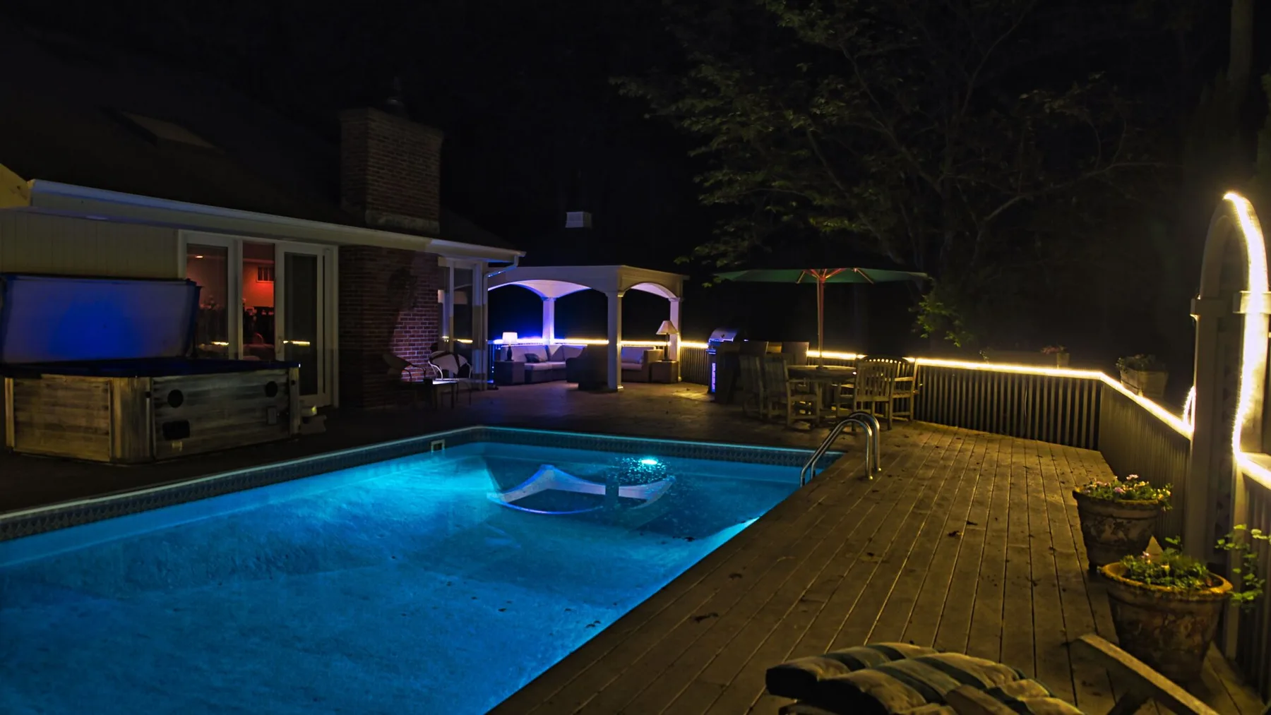 A swimming pool beside a wooden deck, illuminated at night.