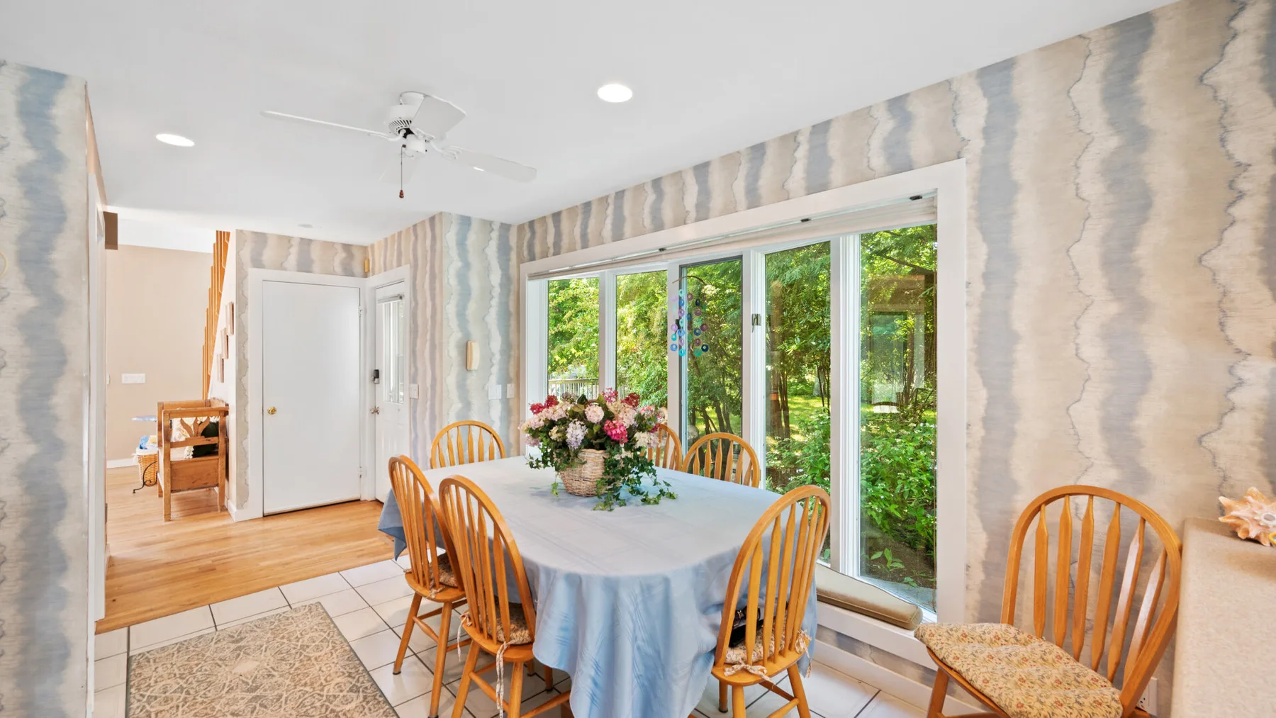 A dining area with a table, wooden seating, and large windows overlooking greenery.