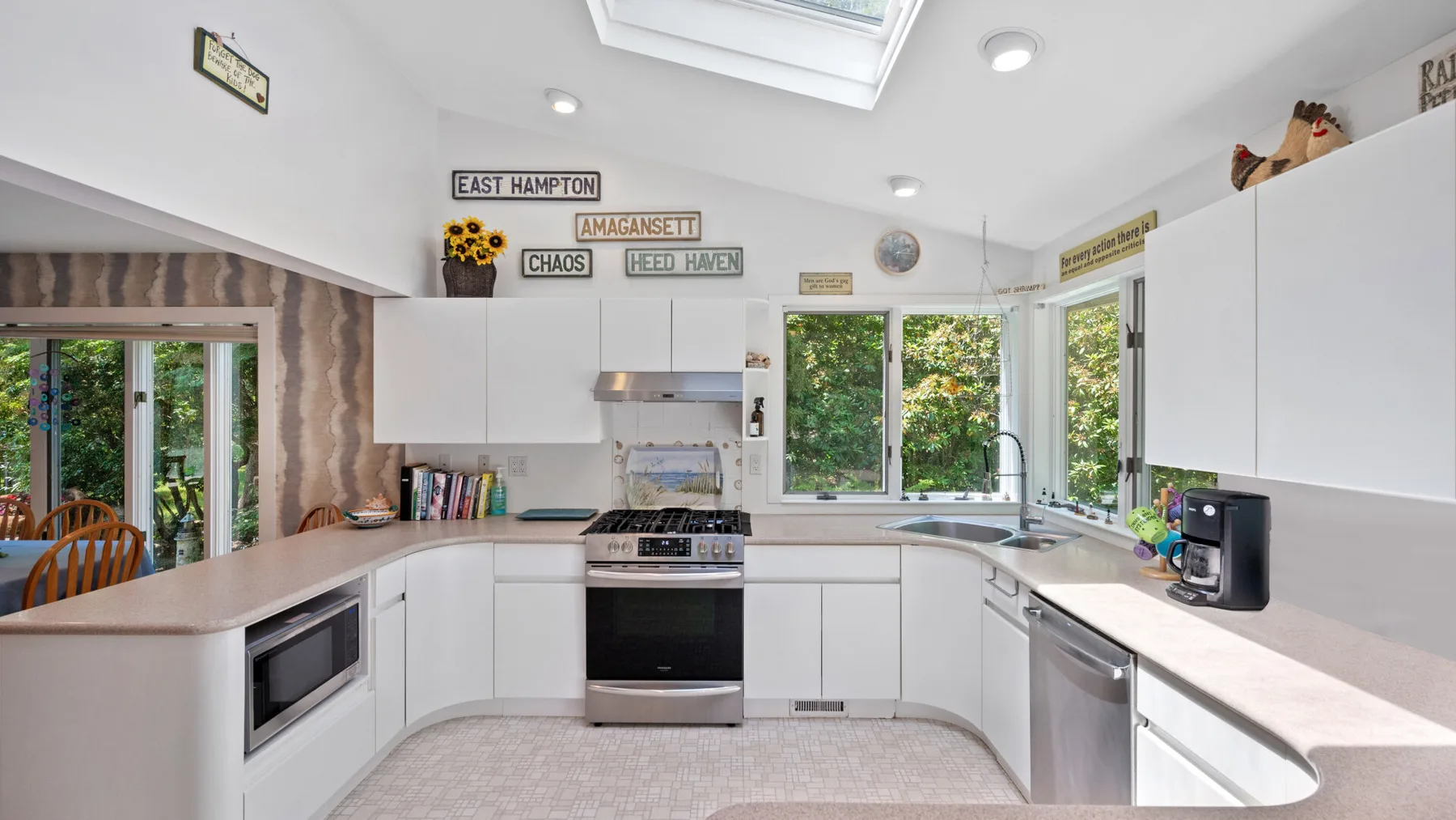 A bright kitchen with white cabinets, a central range, and windows overlooking greenery.