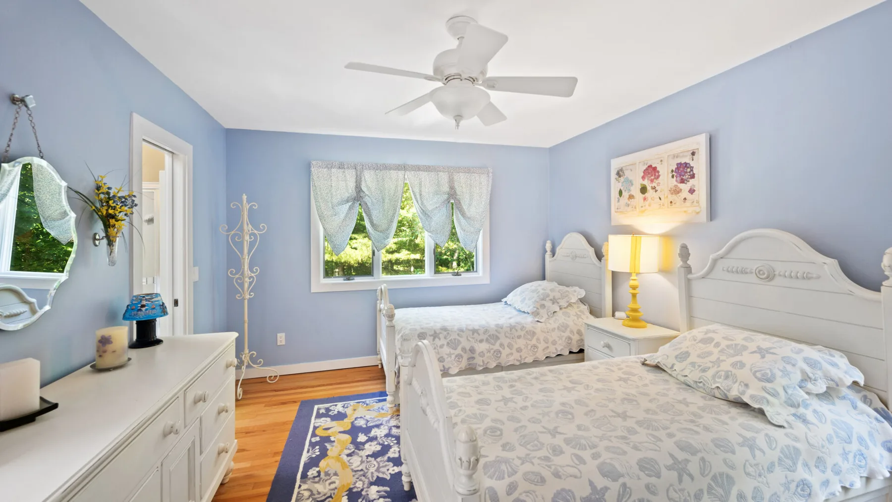 A blue bedroom with two beds and a window overlooking greenery.