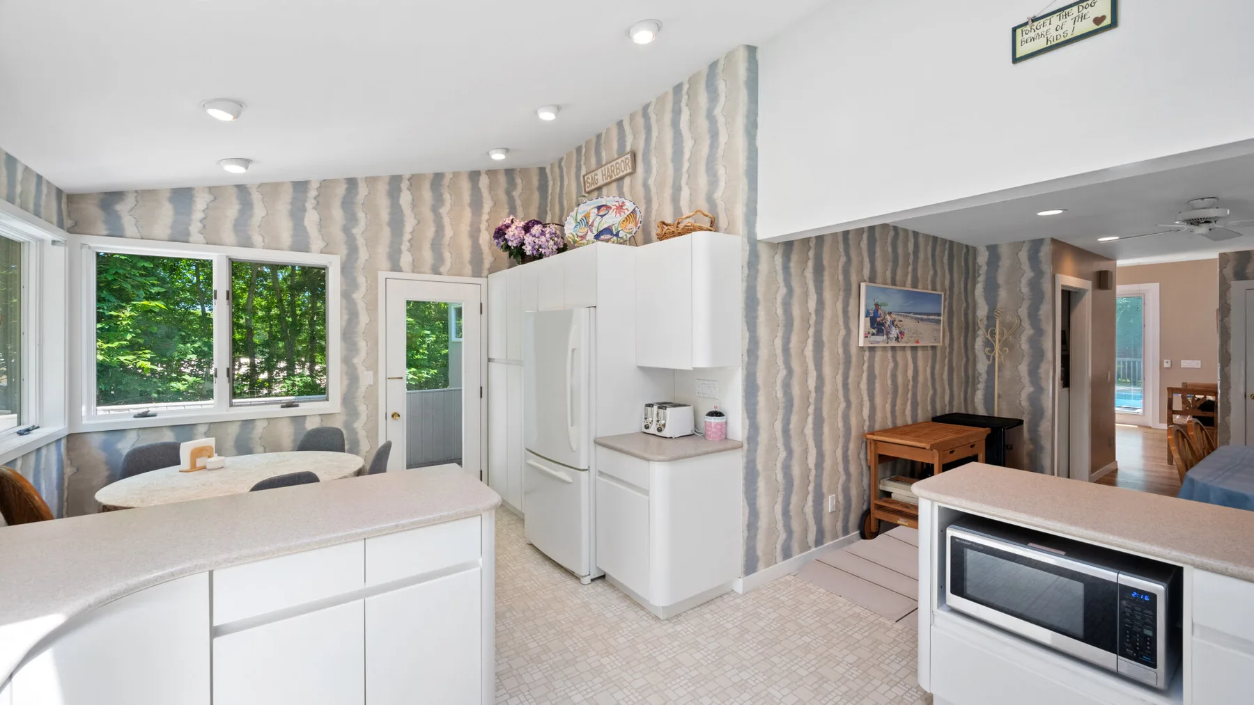 A bright kitchen with white cabinets, a microwave, and windows overlooking greenery.