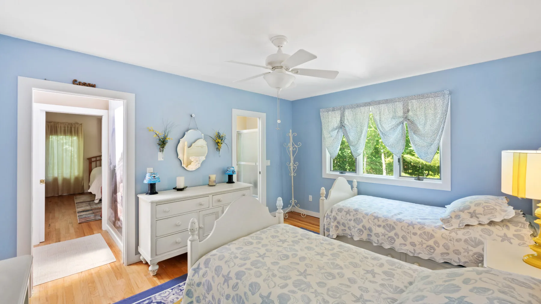 A blue bedroom with two beds and a white dresser.