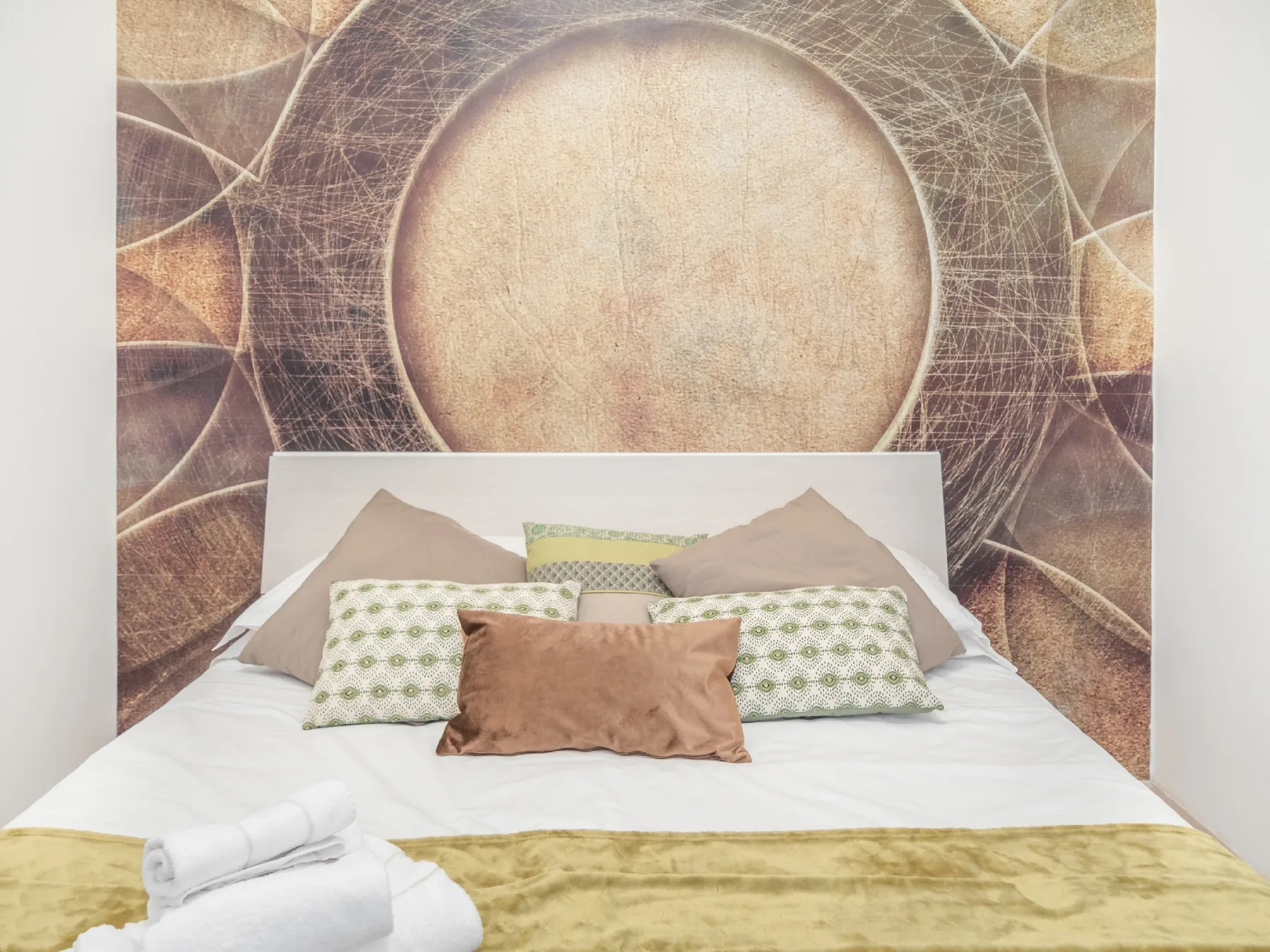 A bedroom with a bed arranged against a large circular wall mural.