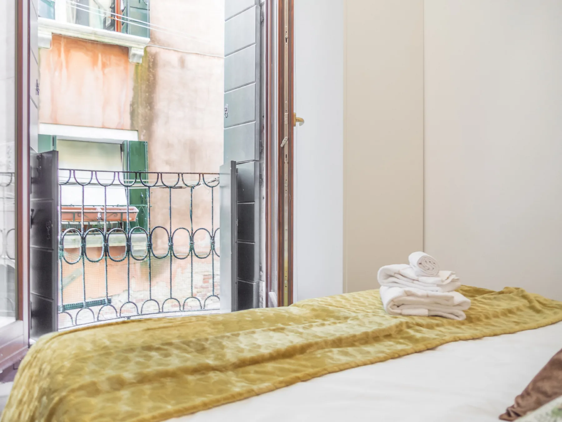 A bedroom with a bed covered by a mustard-colored blanket beside an open window.