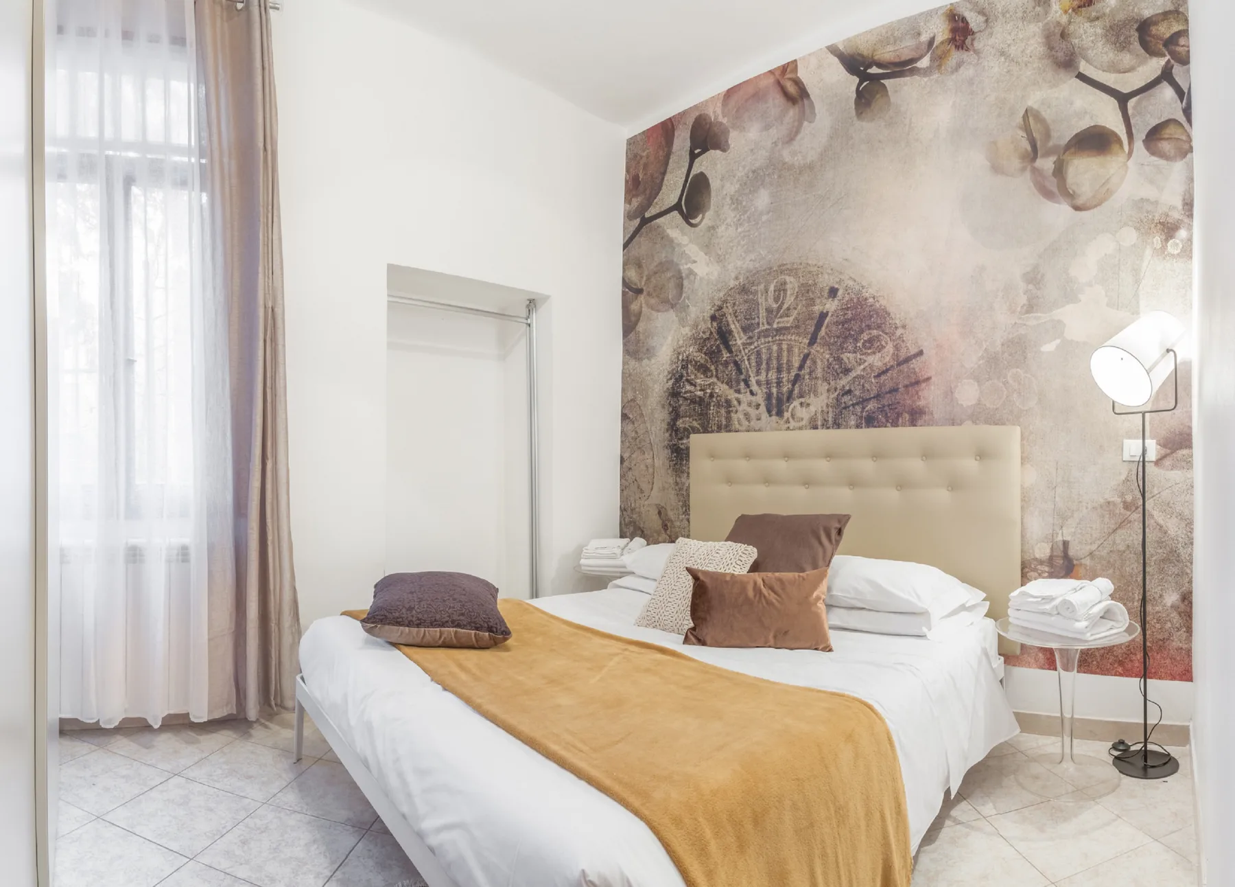 A bedroom with a double bed and a large patterned mural behind the headboard.