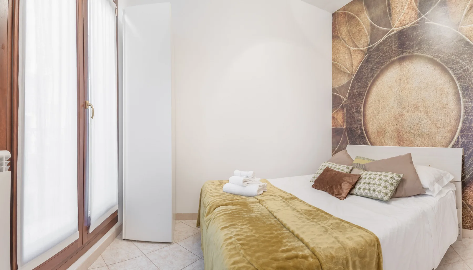 A bedroom with a bed covered by white bedding and a gold blanket.