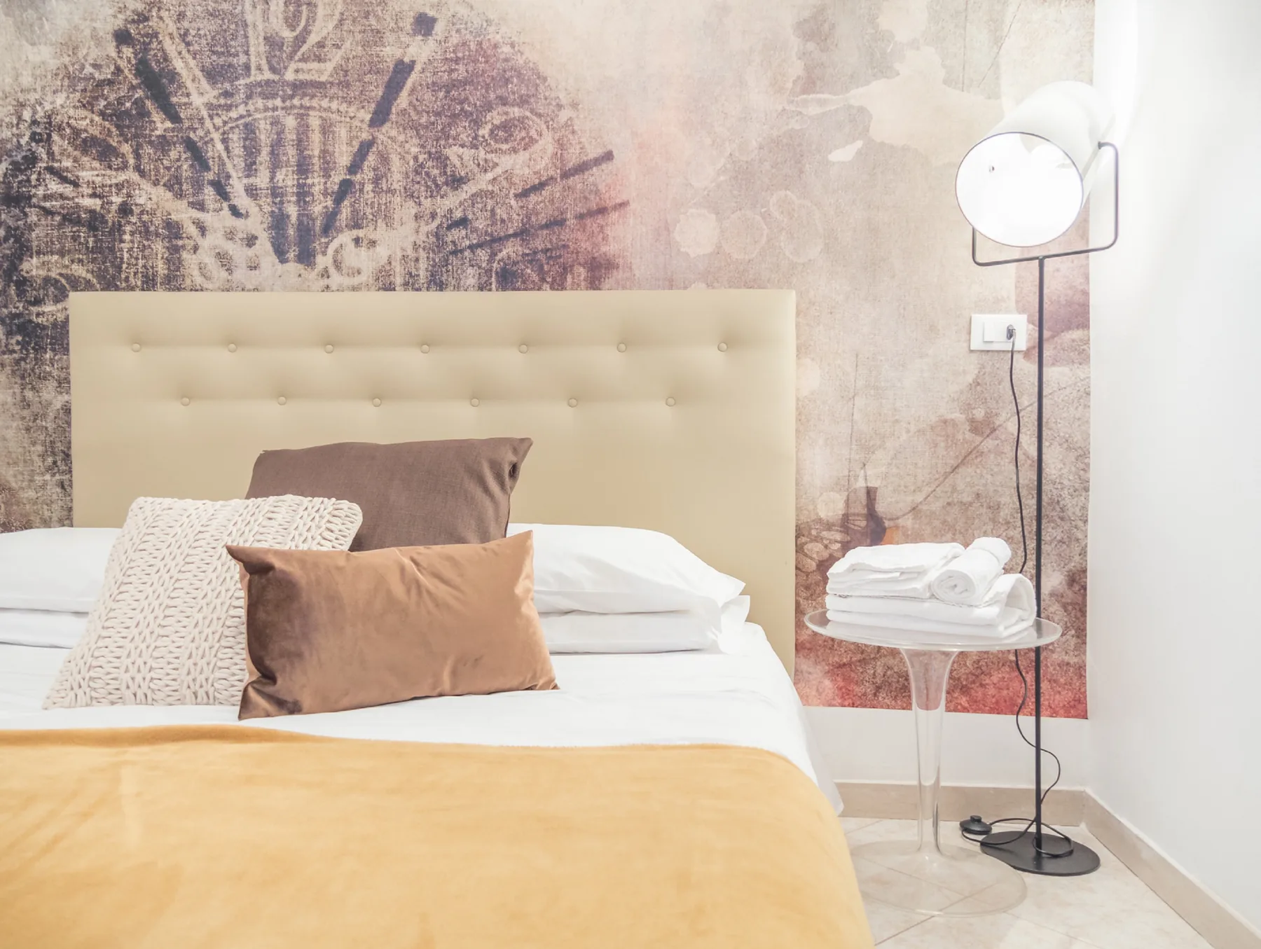 A bedroom with a neatly made bed and a floor lamp beside it.