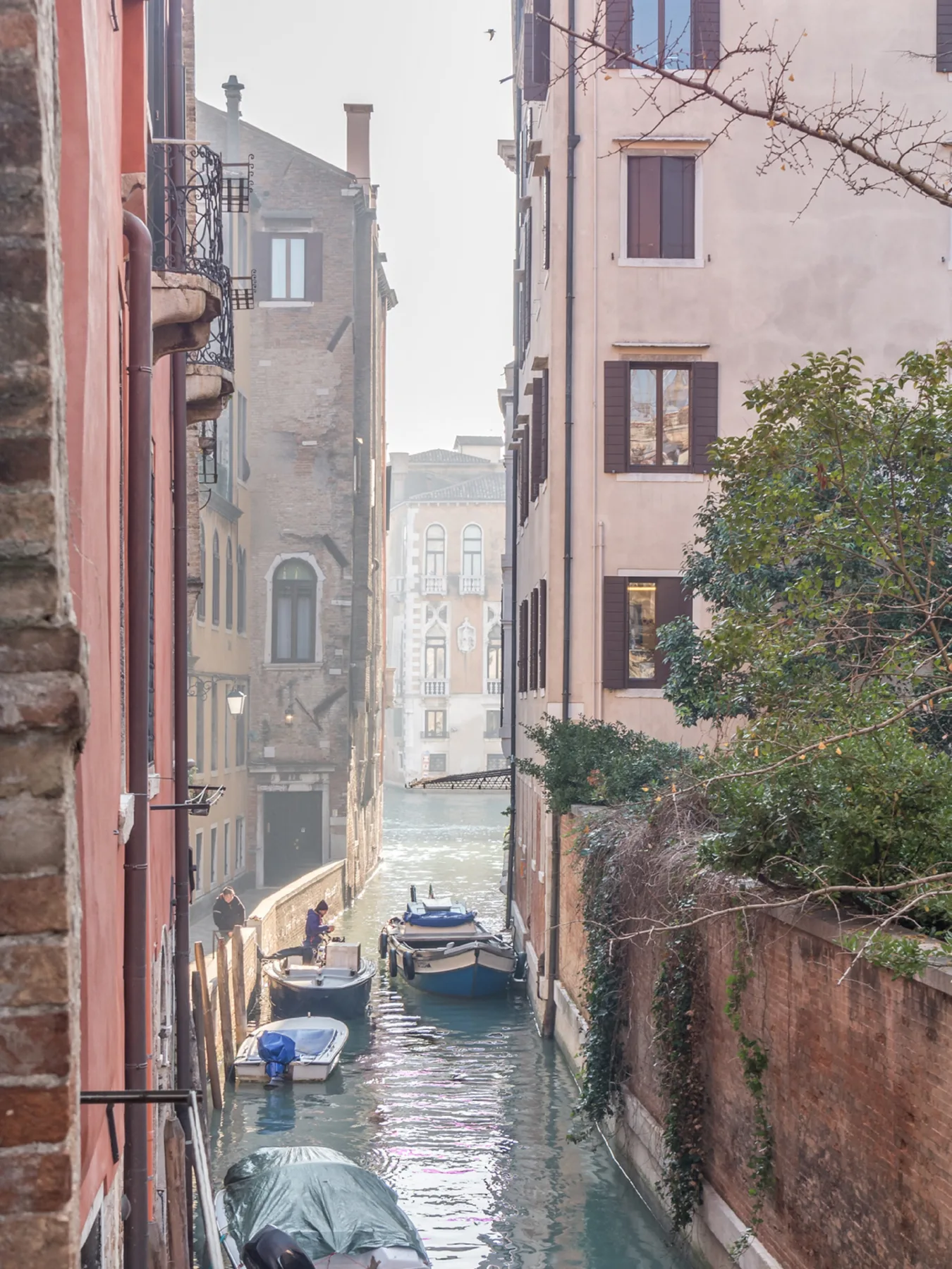 A narrow canal runs between tall buildings, with several boats moored along the water.
