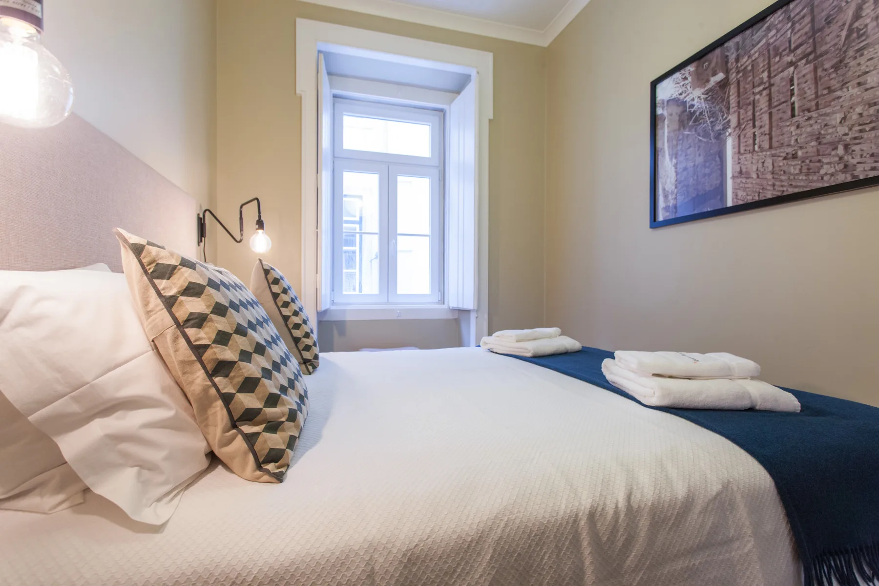 Un dormitorio con una cama bien tendida y una ventana alta.