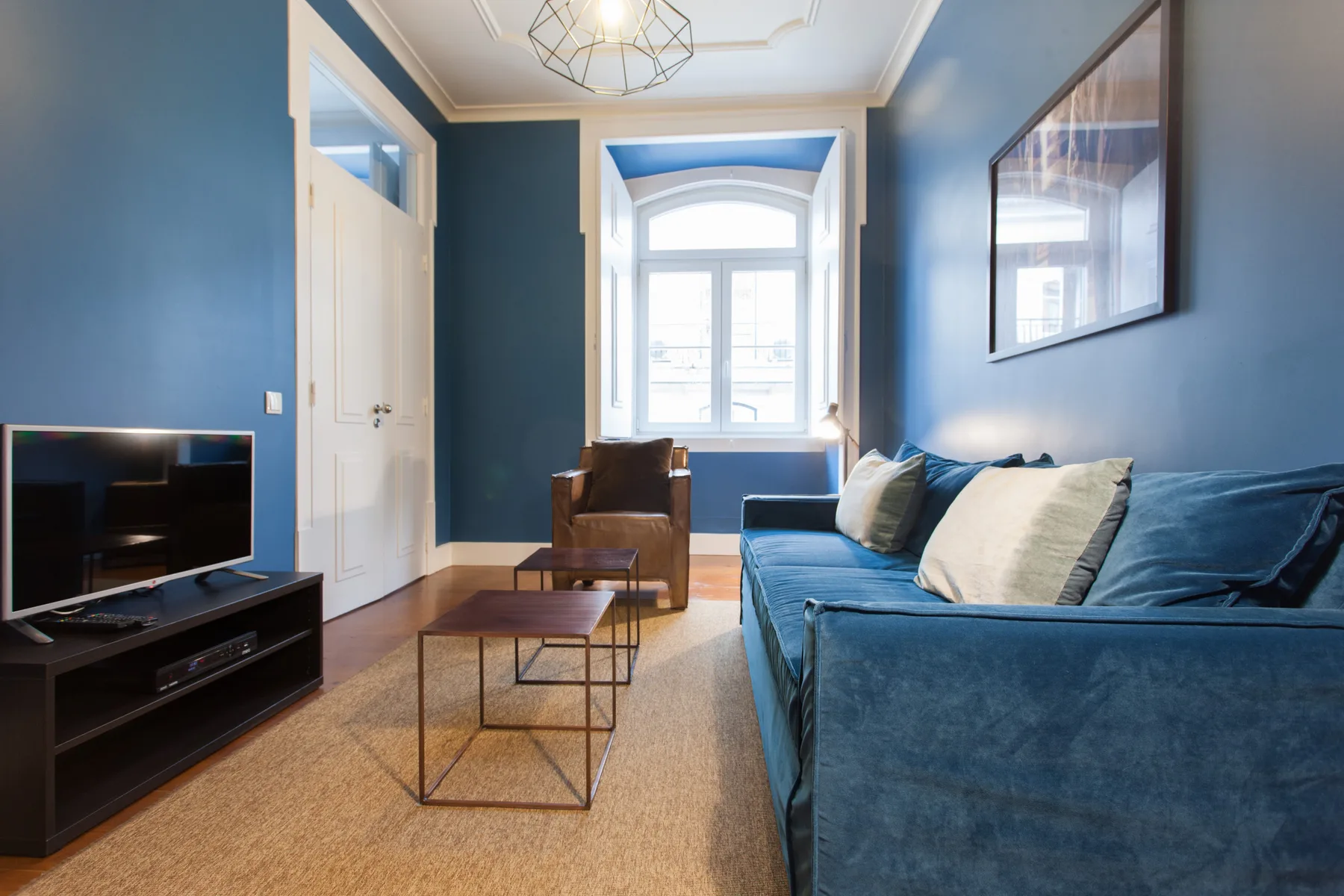 Sala de estar con asientos azules, un televisor y una ventana luminosa.