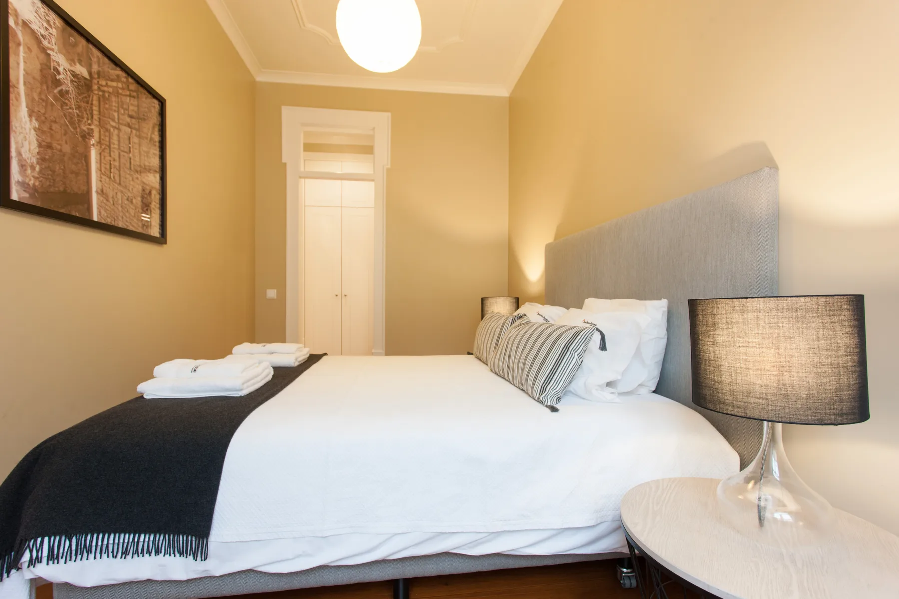 Dormitorio con una cama tendida, lámparas de mesilla y arte enmarcado en la pared.