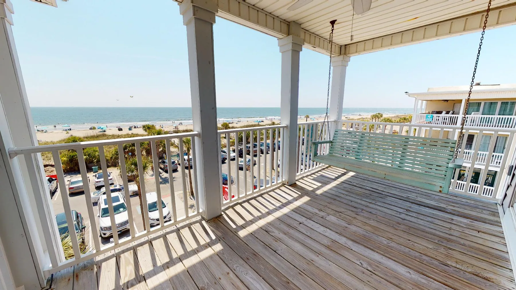 A covered balcony with railing overlooks parked cars and the ocean.