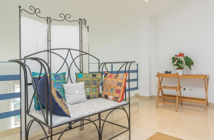 A bright room with a metal daybed, colorful cushions, and a small desk.