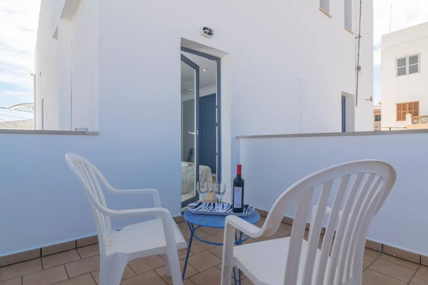 A small outdoor seating area with white chairs and a table beside an open doorway.