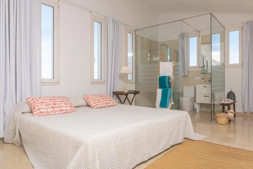 A bright bedroom with a bed beside a glass-enclosed shower area.