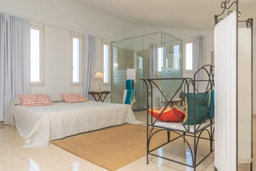 A bright bedroom with a large bed, a glass shower, and a woven rug.