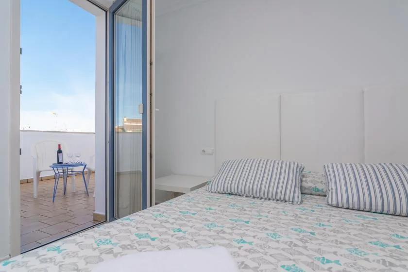 A bright bedroom with patterned bedding beside an open glass door to a balcony.