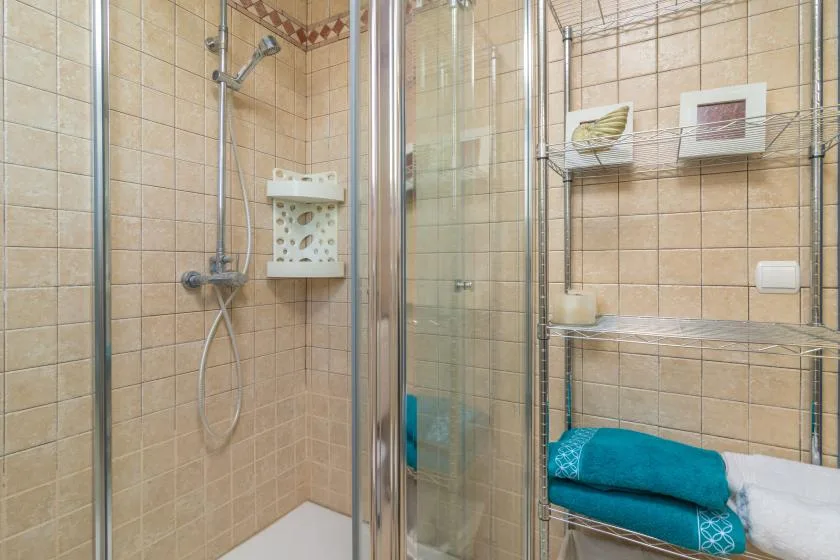 A tiled bathroom with a glass shower and metal shelving.