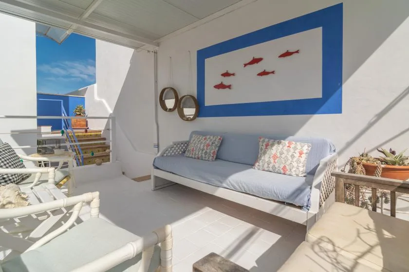 A bright covered patio with cushioned seating and a blue-framed fish artwork.