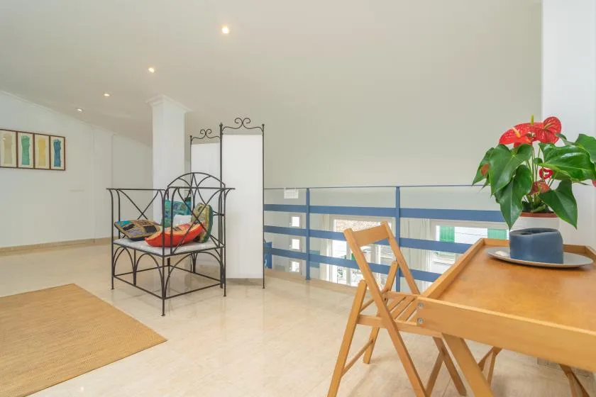 A bright sitting area with a metal bench, wooden table, and blue railing.
