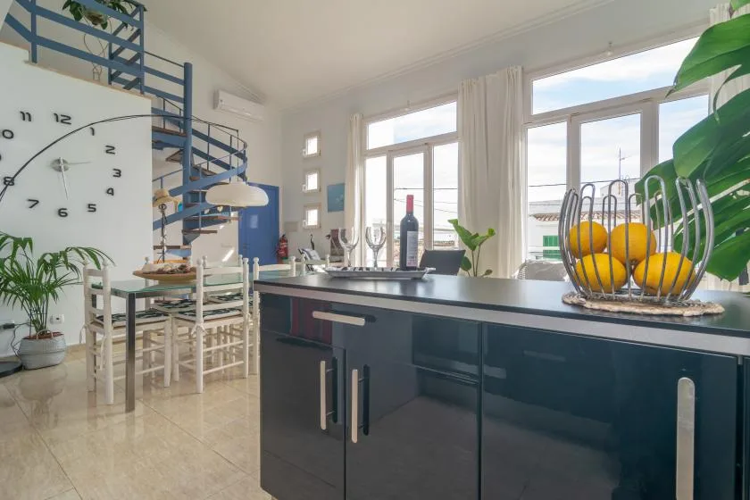 A bright kitchen with a dark island, dining table, and large windows.