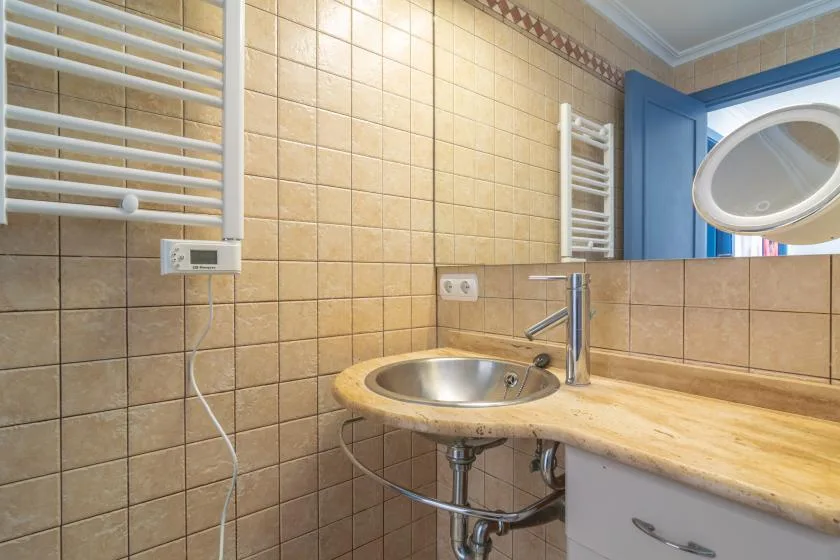 A tiled bathroom with a sink, countertop, and wall-mounted towel warmers.
