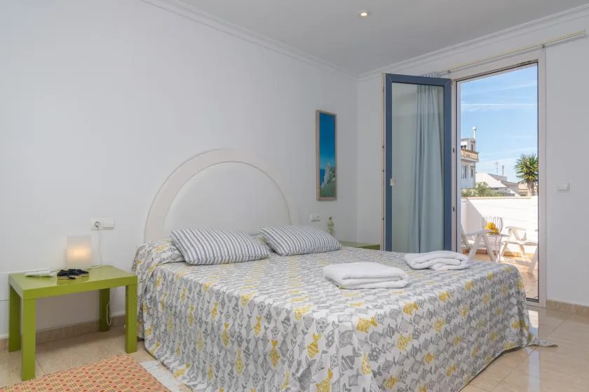 A bright bedroom with a double bed and an open door leading to a balcony.