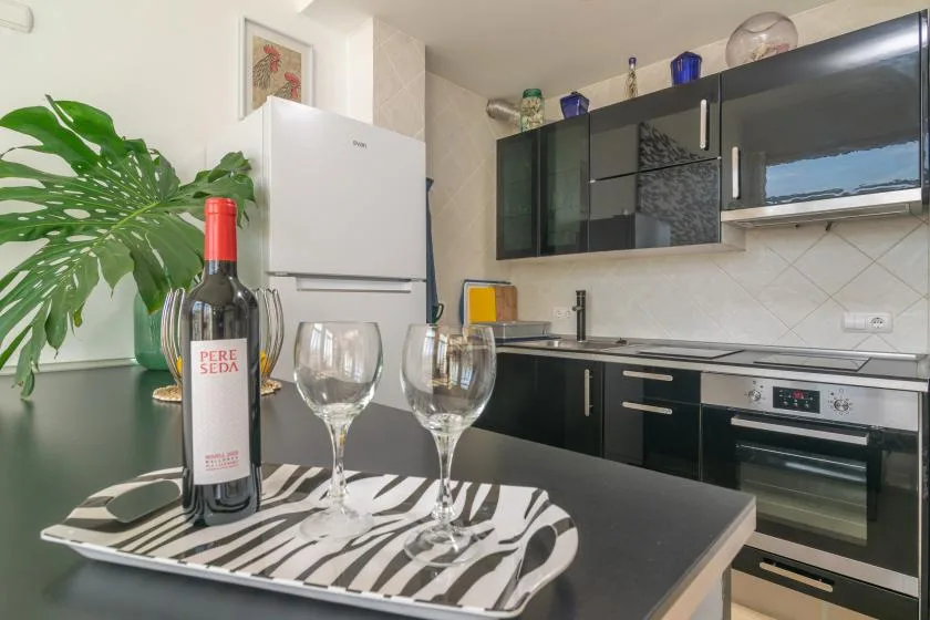A kitchen with dark cabinets, a refrigerator, and a wine bottle with glasses on the counter.