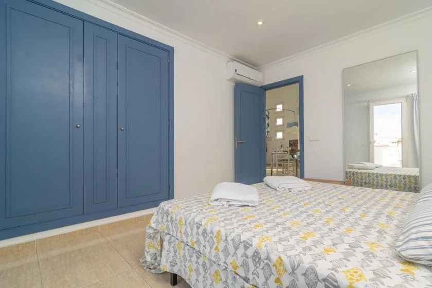 A bedroom with a bed covered in patterned bedding and blue built-in wardrobes.