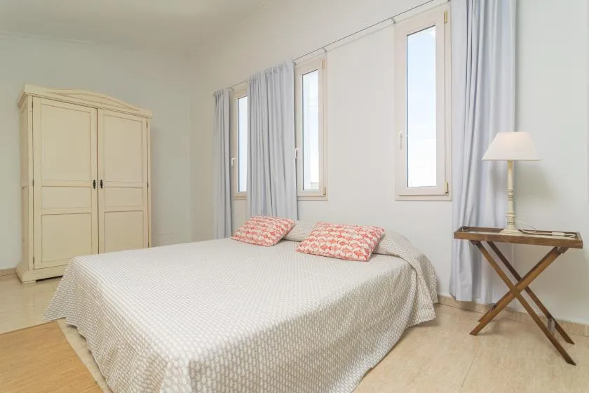 A bright bedroom with a large bed, curtained windows, and a bedside table.