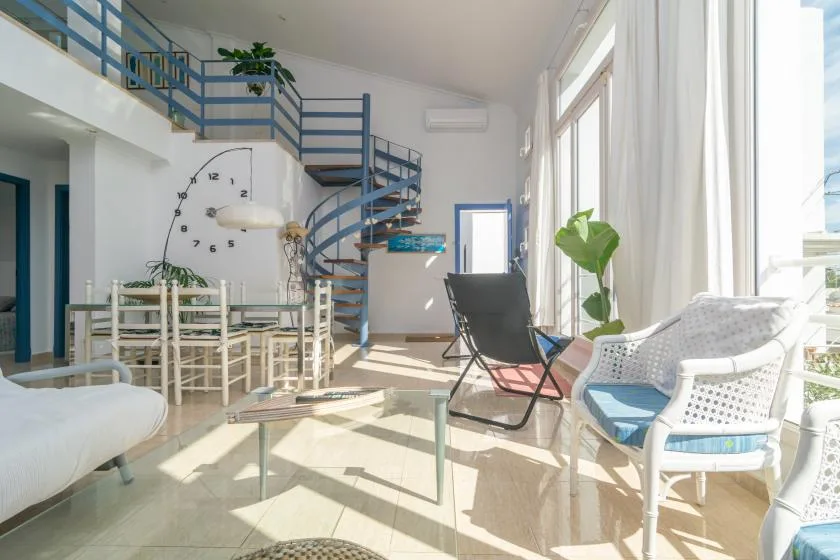 A bright living and dining area features a spiral staircase and seating by large windows.
